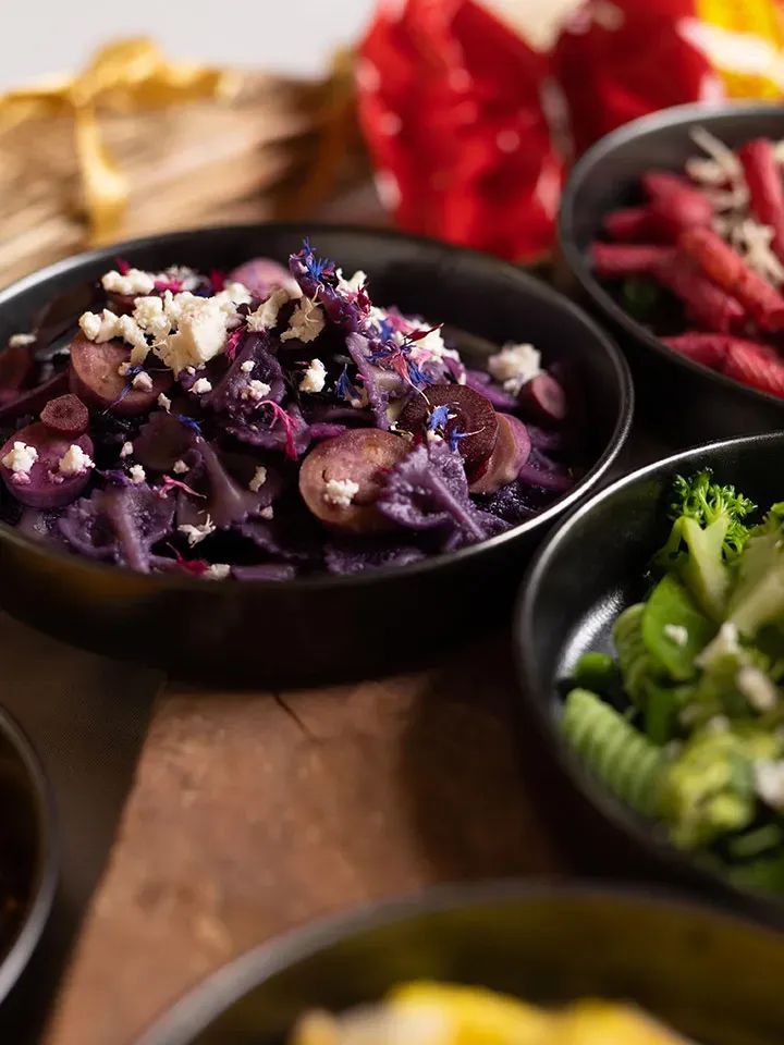 Purple Pasta mit Rotkohlsauce: Schüssel mit lila Gemüse und weißem Käse auf Holztisch neben weiteren Schüsseln