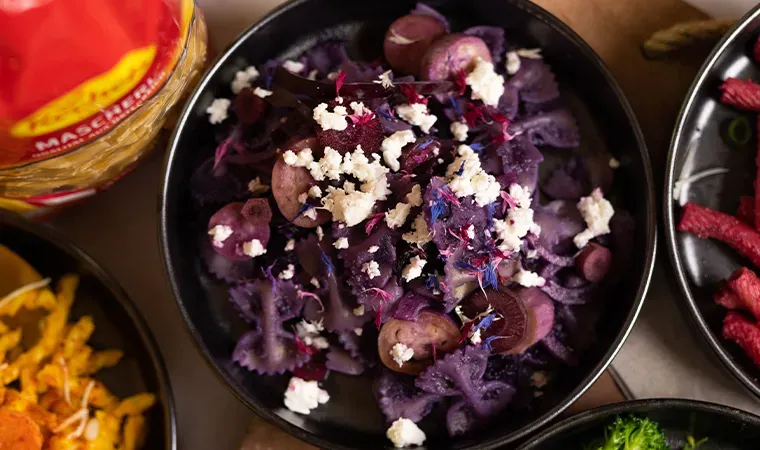 Purple Pasta mit violetten Karotten, Pilzen und weißem Käse in einer Schüssel auf einem Tisch