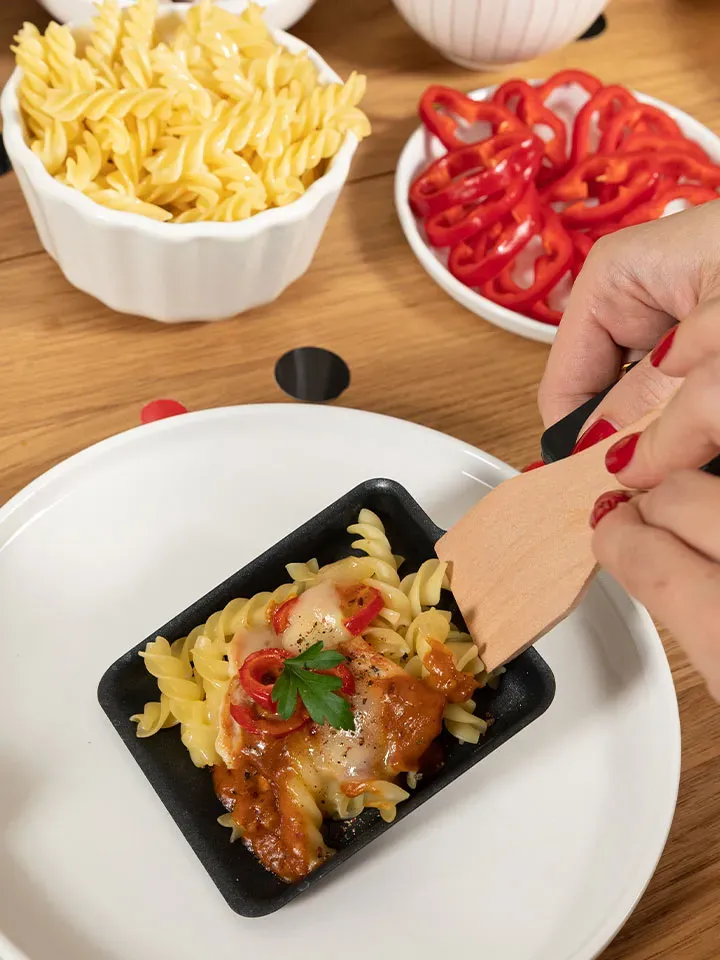 Hand serviert Raclette mit Huhn als Nudelauflauf mit Paprika und Käse aus einem kleinen Pfännchen auf einen Teller