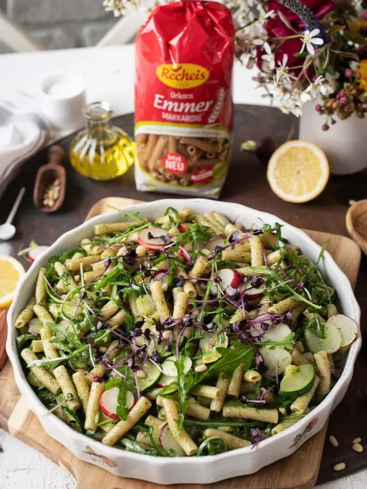 Emmer-Makkaroni-Salat mit Radieschen-Grünpesto, Gemüse und Kräutern auf einem Teller auf Holzbrett