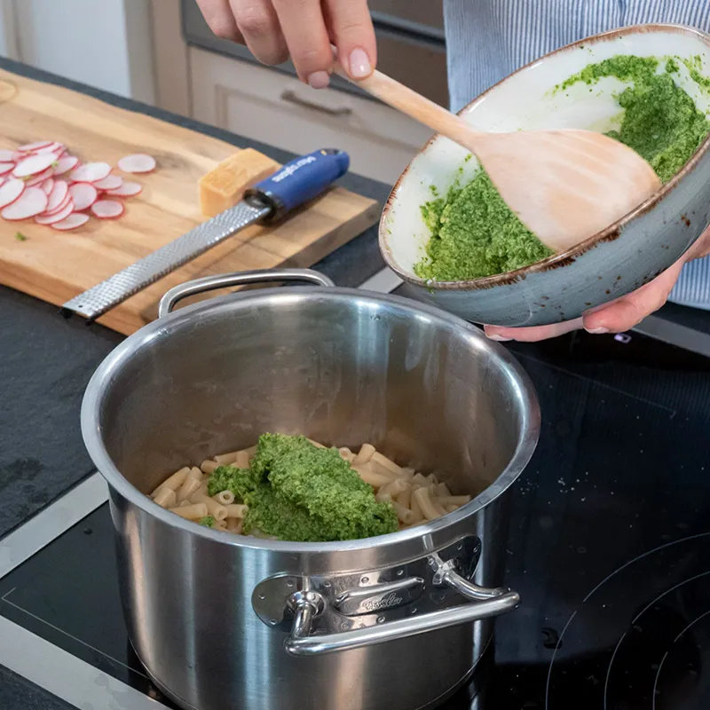Radieschenpesto selber machen: Person rührt grüne Kräuter und geriebenen Käse in einer Schüssel