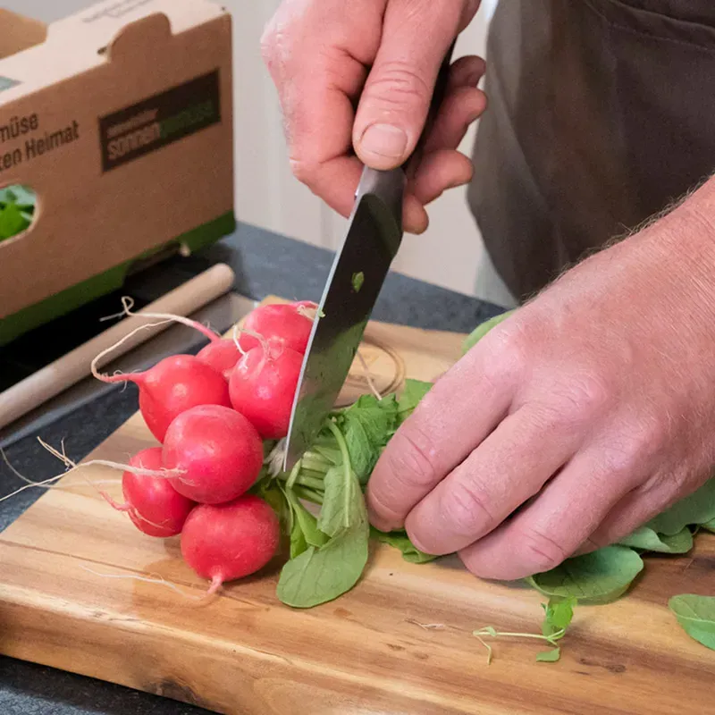 Radieschenpesto selber machen: Hände schneiden Radieschen auf Holzbrett in der Küche