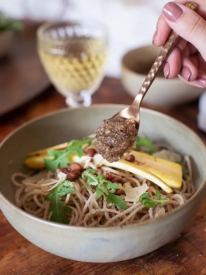 Hand hält einen Löffel mit selbstgemachtem Nusspesto über einer Schüssel mit Recheis Emmer Spaghetti und Gemüse