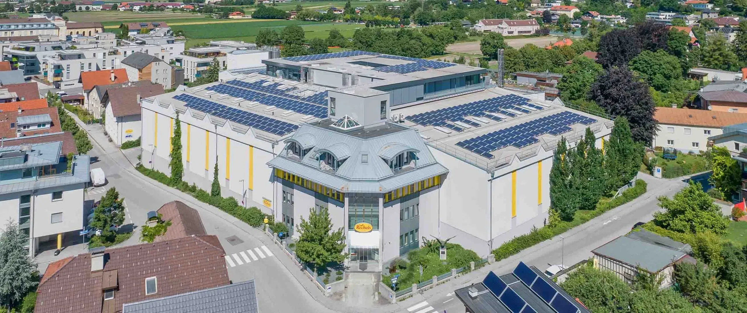Luftaufnahme des Recheis-Gebäudes mit Solarpaneelen auf dem Dach in einer Wohngegend, Sommer 2021