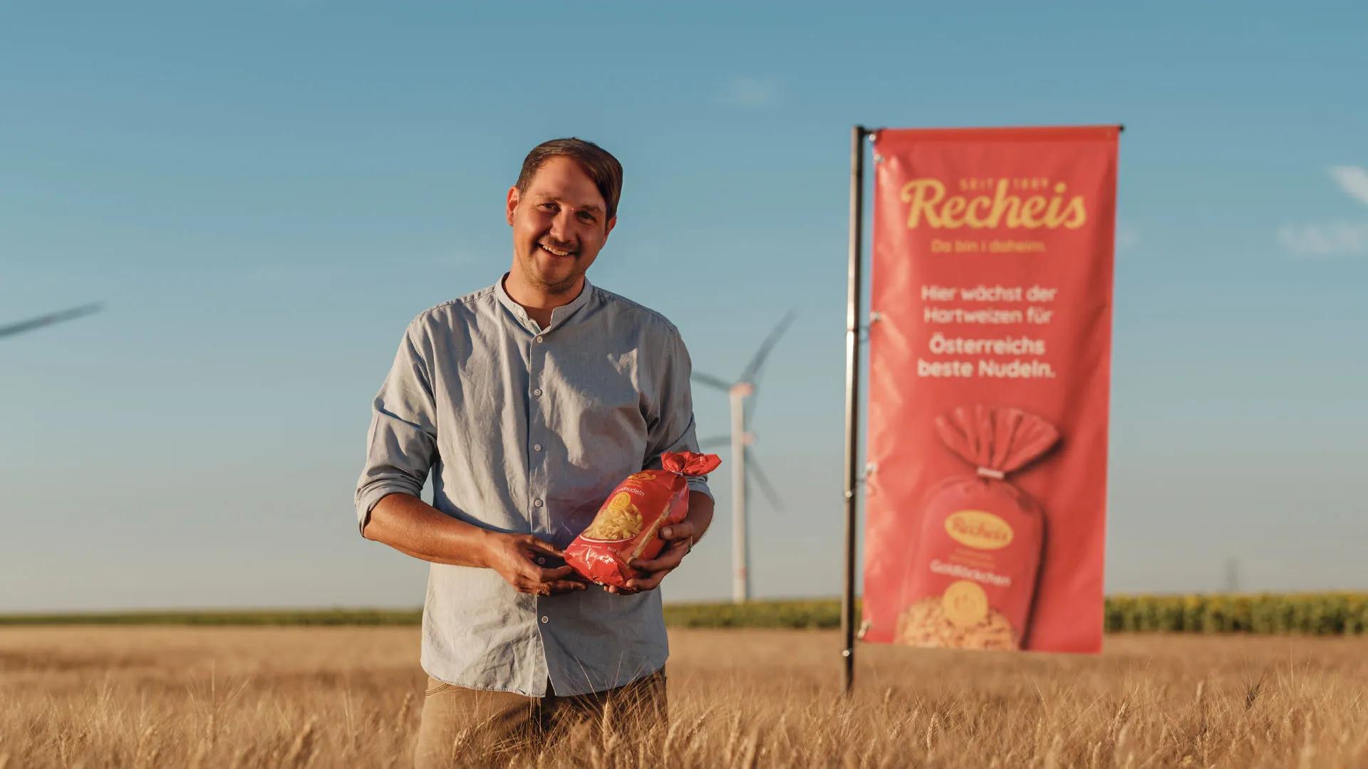 Mann hält Nudeln auf Feld mit Windrädern und Werbebanner im Hintergrund
