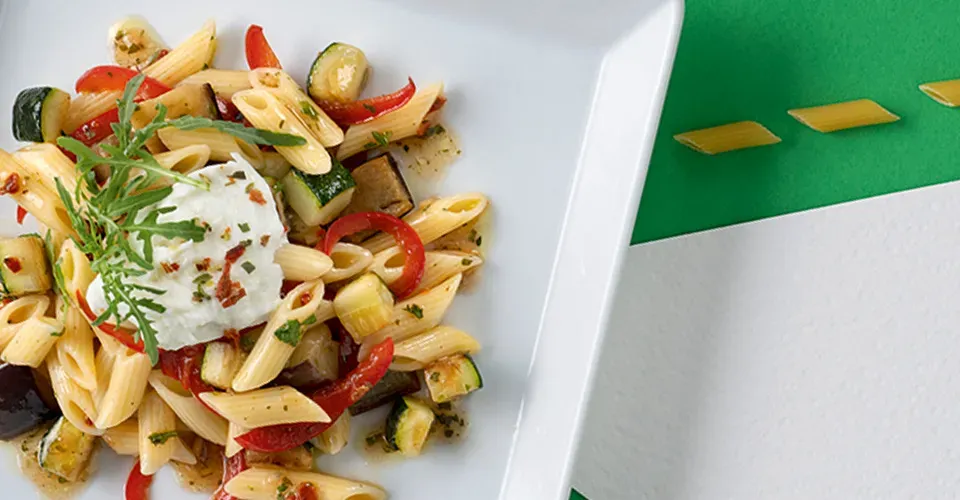 Nahaufnahme: Penne mit Gemüse, Mozzarella und Rucola auf einem Teller