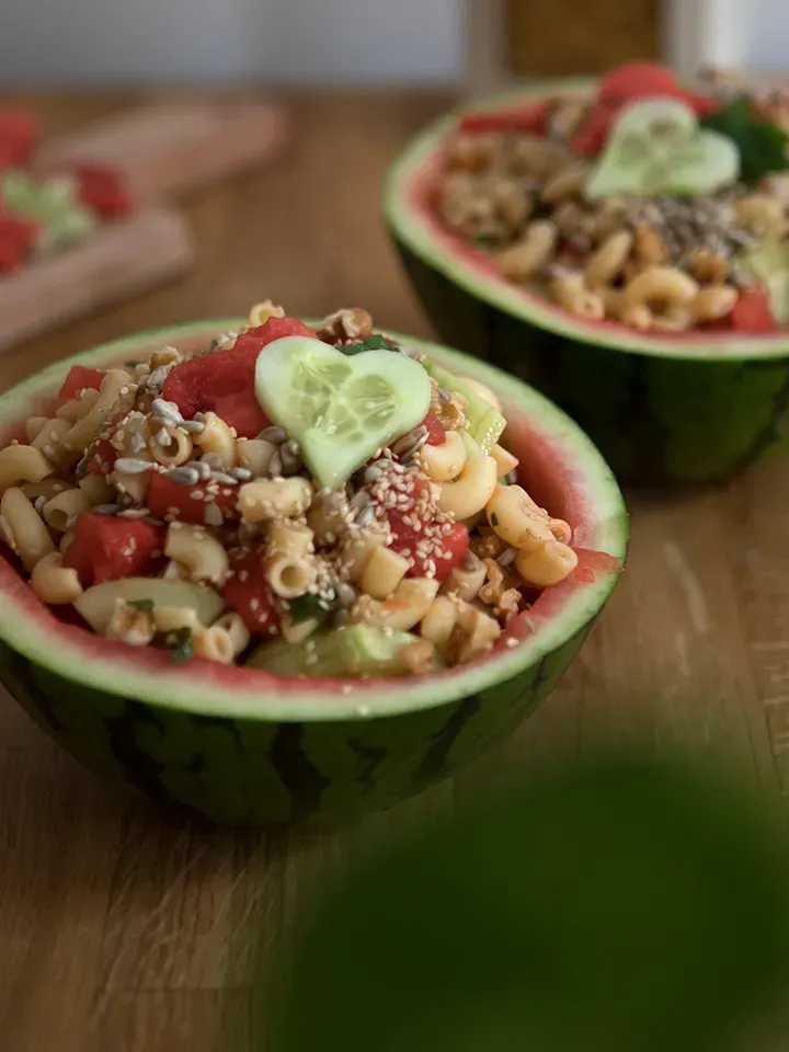 Veganer Nudelsalat mit Gemüse in einer ausgehöhlten Wassermelone, mit Gurkenherz garniert