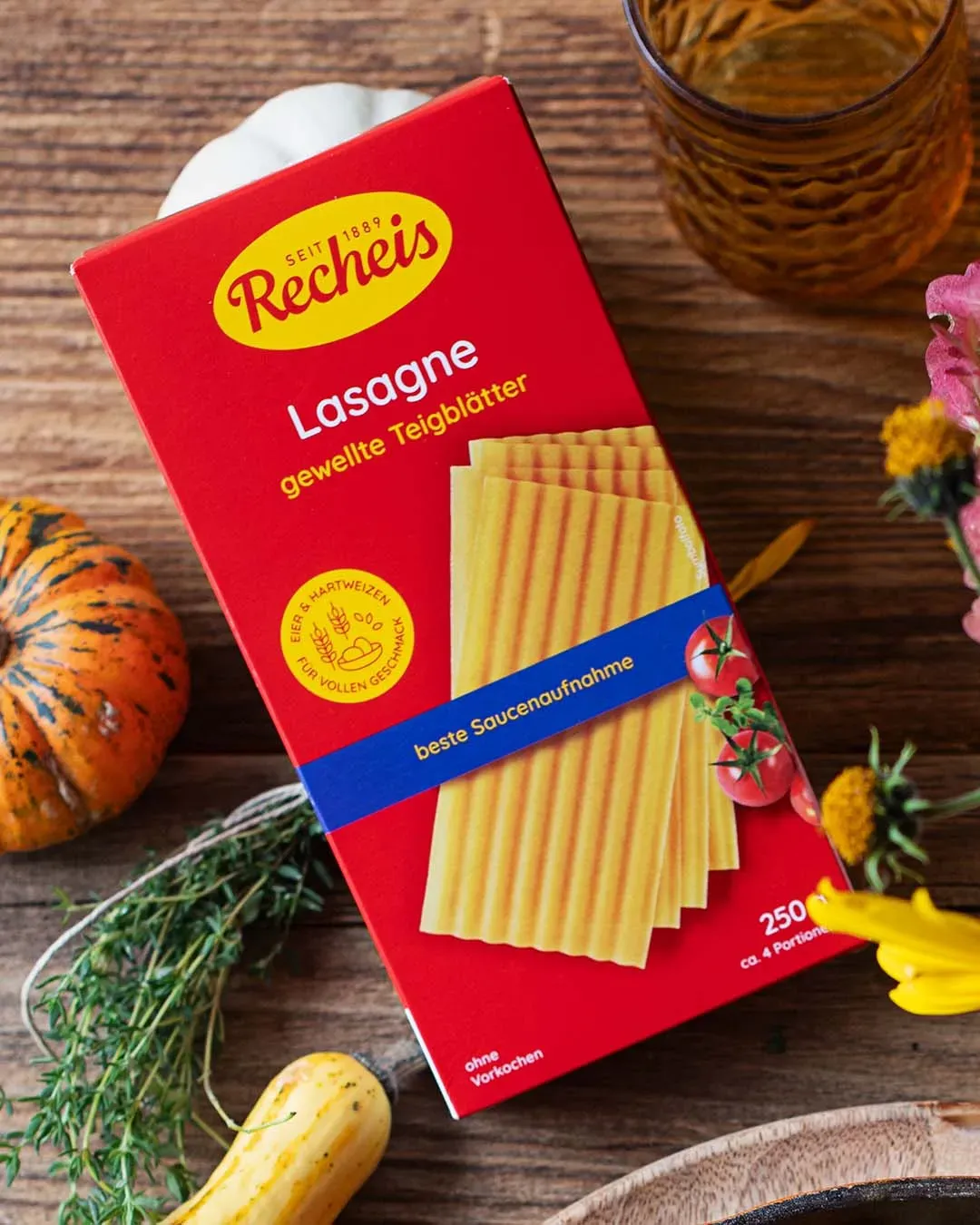 Packung Recheis Lasagne mit gewellten Teigblättern ohne Vorkochen auf Holztisch mit Gemüse und Glas
