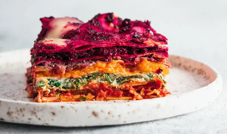 Bunt geschichtete Regenbogen-Cashew-Lasagne mit Gemüse auf einem weißen Teller