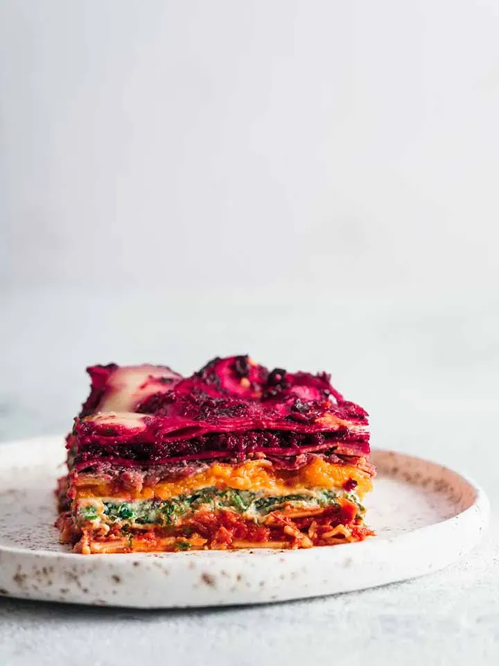 Stück Regenbogenlasagne mit Cashew und verschiedenen Gemüseschichten auf einem weißen Teller