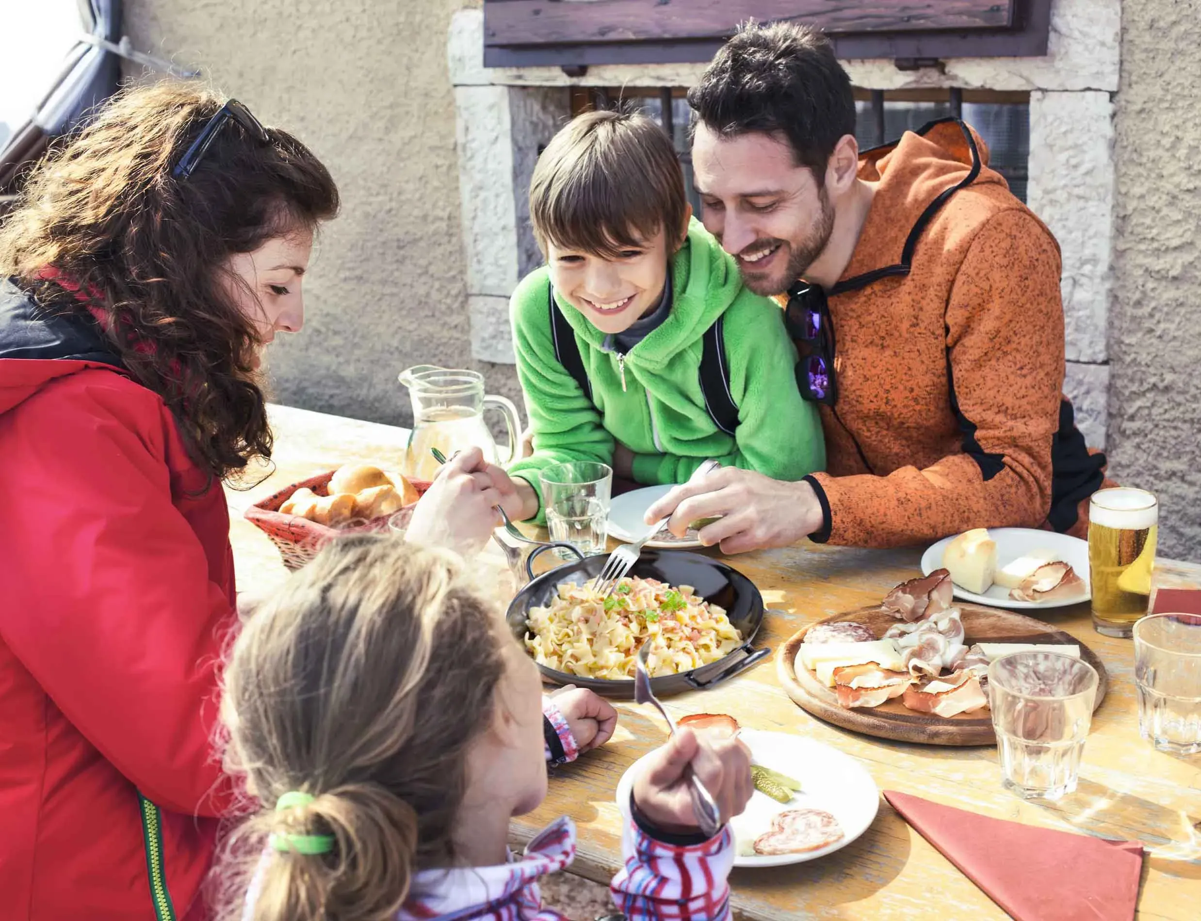 Familie isst gemeinsam draußen an einem Holztisch mit verschiedenen Speisen