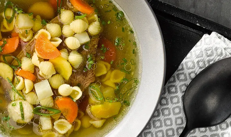 Alt-Wiener Suppentopf mit Muscheln: Gemüsesuppe mit Nudeln in einer Schüssel neben einem Löffel auf Stoffserviette