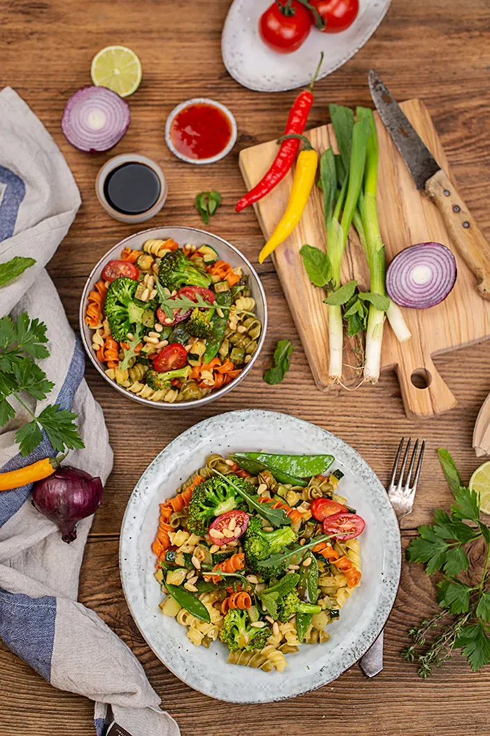 Asia-Nudelsalat mit Recheis Bunte Rollini, Brokkoli, Tomaten und Frühlingszwiebeln auf Holztisch