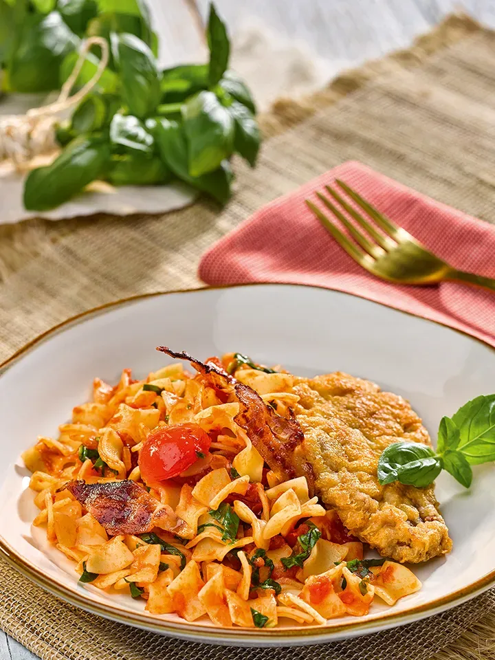 Bio-Fleckerl mit Lamm-Piccata und Bärlauch, mit gebratenem Schnitzel und Basilikumblatt auf einem Teller