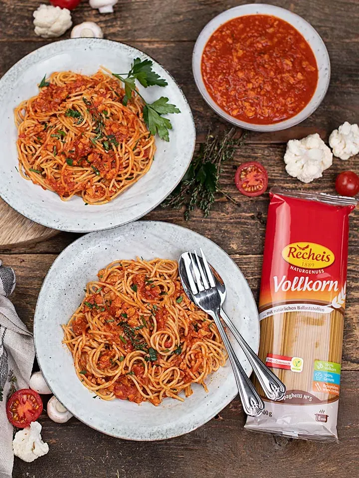 Zwei Teller Vollkornspaghetti mit Karfiol-Bolognese und Kräutern auf Holztisch