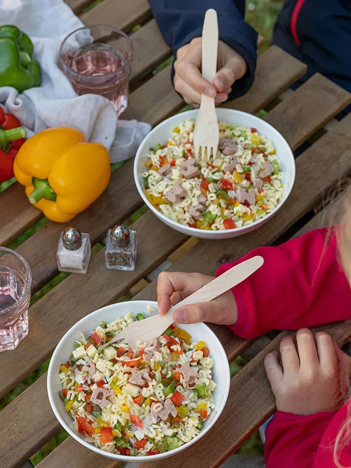 Kinder essen im Freien Buchstabennudelsalat mit Frischkäsedressing, buntem Gemüse und Wurststücken