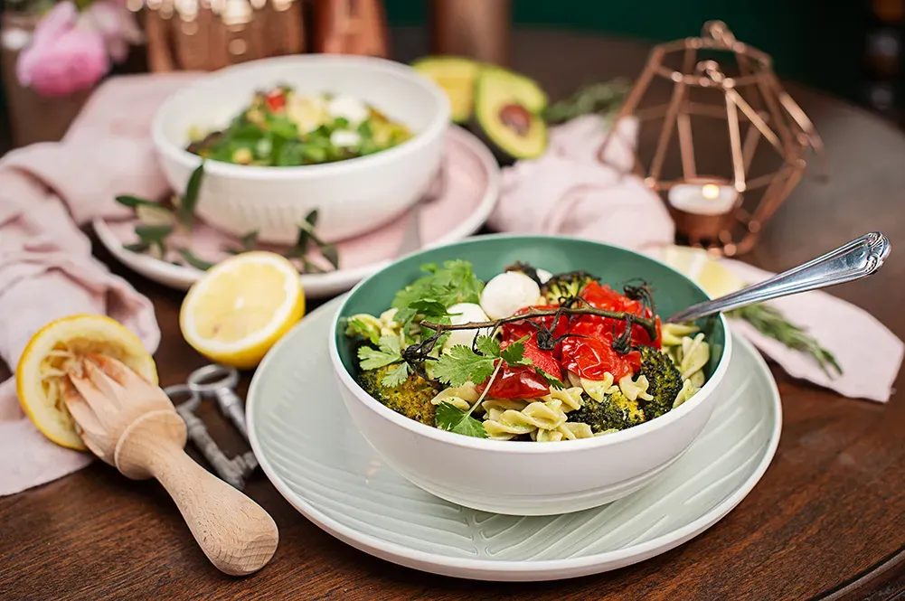 Buddha Bowl mit Vollkornnudeln, Avocado-Buttermilch-Sauce, Brokkoli, Tomaten und Kräutern, daneben Zitrone und Kerze