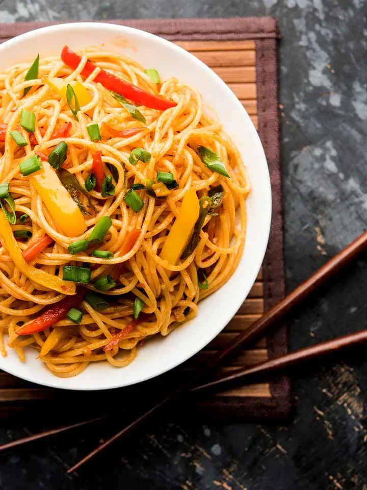 Chow Mein mit gebratenen Nudeln und buntem Gemüse auf einem Teller, daneben Essstäbchen