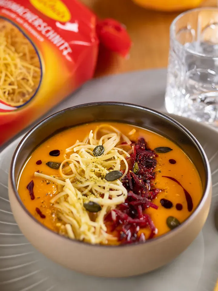 Cremige Kürbissuppe mit Hausmacherschnitt in einer Schüssel, mit Käse, Roter Bete und Kürbiskernen garniert