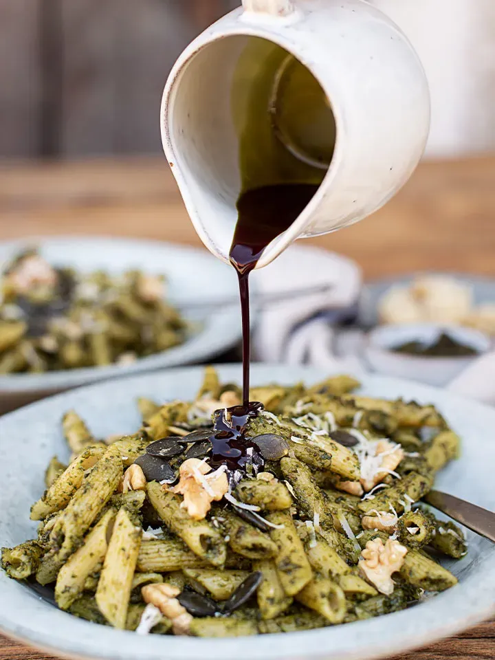 Dinkelpenne mit Bärlauch-Kürbiskernpesto, Walnüssen und Kürbiskernen, die mit dunkler Sauce übergossen werden