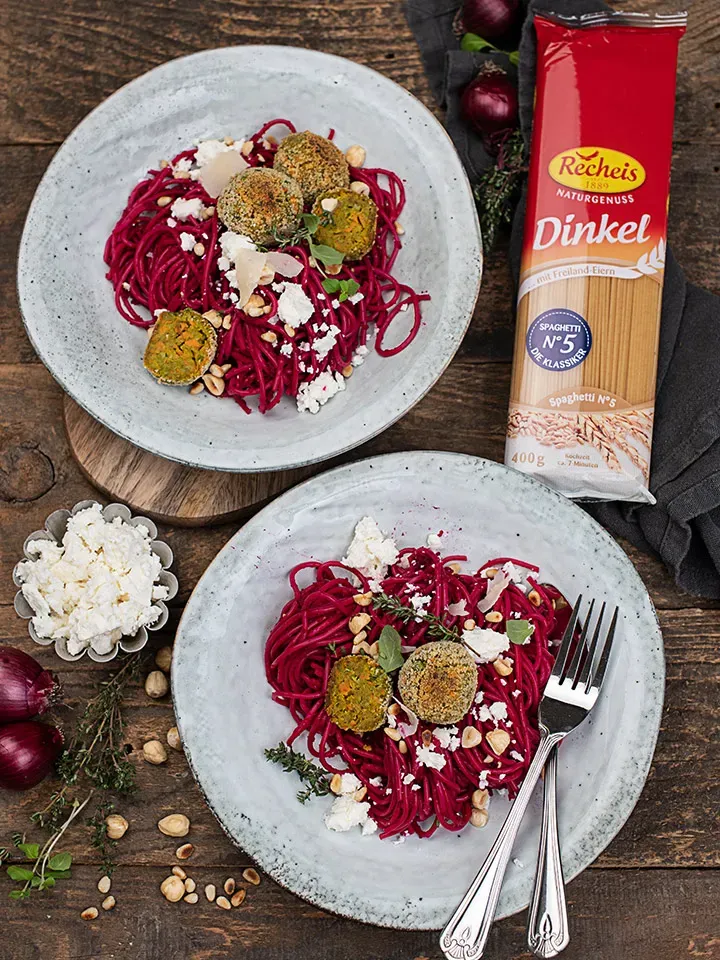 Dinkelspaghetti mit Rote-Rüben-Sauce, Gemüsebällchen und Feta auf zwei Tellern neben der Dinkel-Spaghetti-Packung