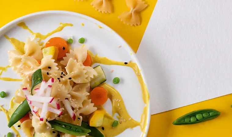 Farfalle mit glasiertem Gemüse, Sesam und Kresse in gelber Sauce auf gelbem Hintergrund