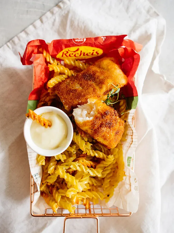 Panierte Fischfilets mit Nudelchips aus dem Backofen und Sauce in einem Drahtkorb serviert