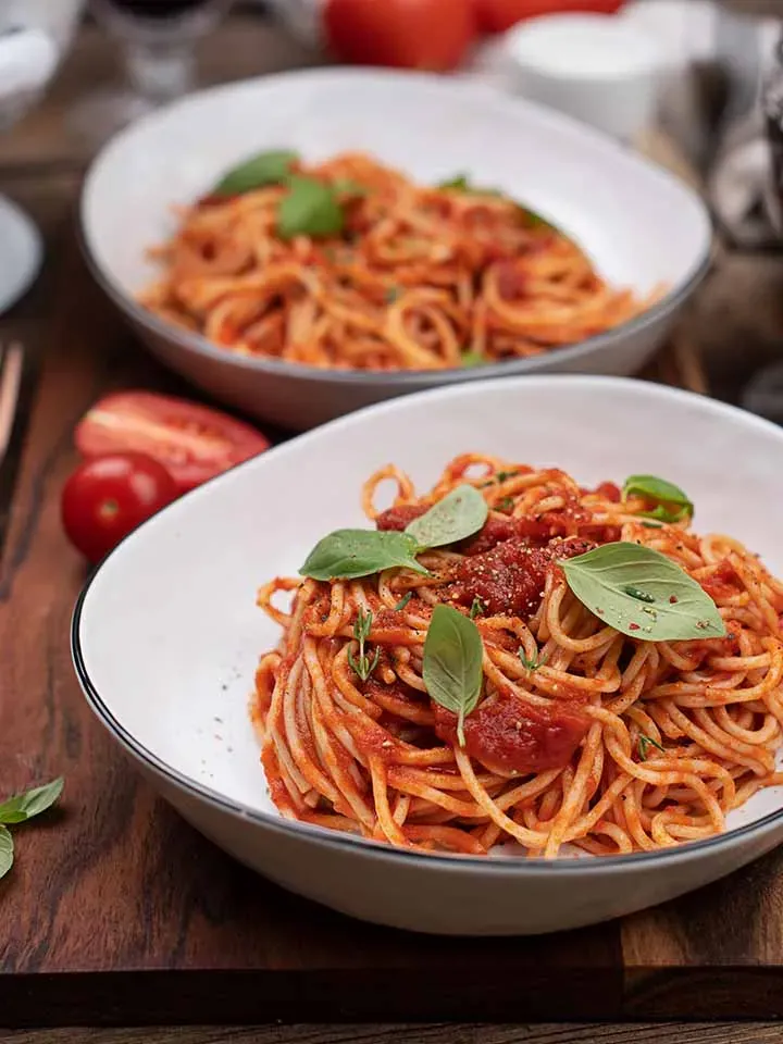 Selbstgemachte Tomatensauce: zwei Schalen Spaghetti mit Basilikum auf einem Holzbrett
