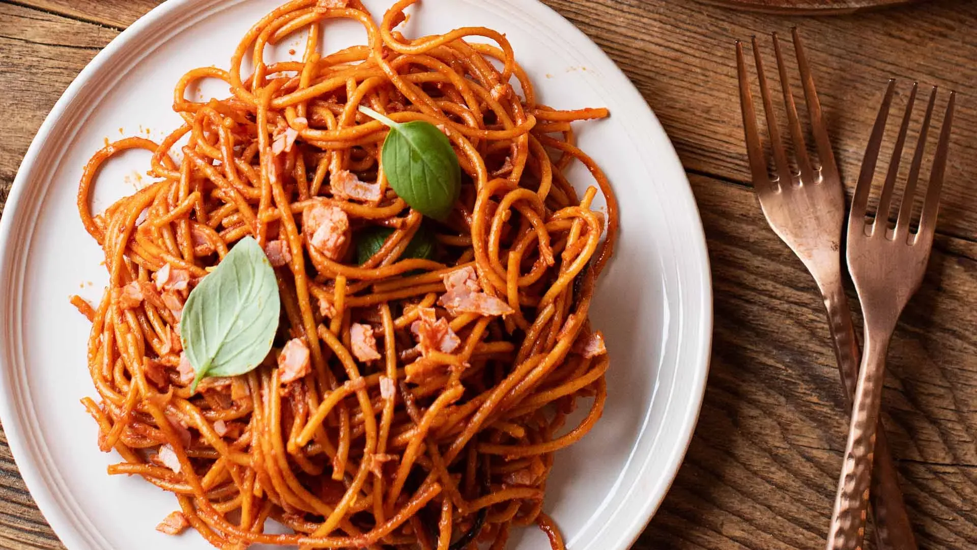 Gebratene Spaghetti in Tomatensauce auf einem Teller, mit Basilikumblättern garniert, dazu zwei Gabeln