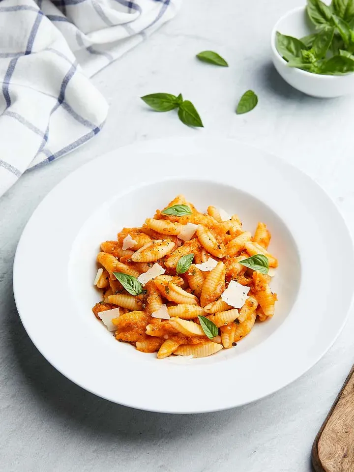Bio-Gnocchi sardi in Tomatensauce mit Basilikum und Parmesan auf einem Teller, Gemeinschaftsverpflegung