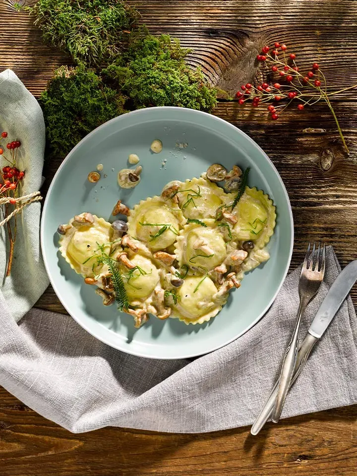 Girasoli mit Steinpilz auf Waldpilzsauce, auf einem Holztisch mit Besteck und Dekoration