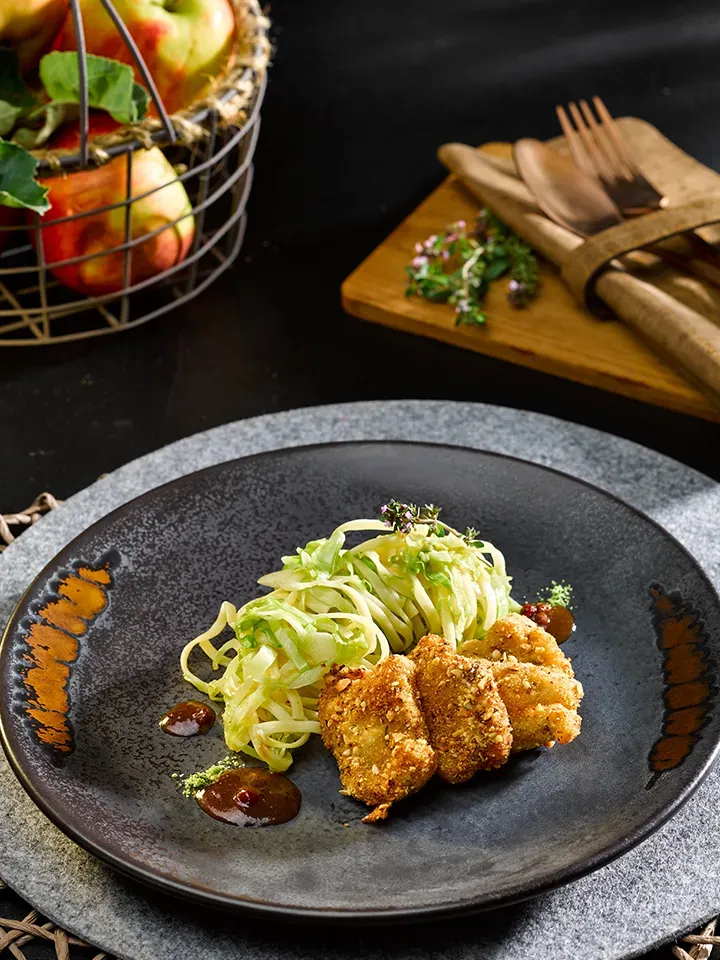 Hirschschnitzel mit grünen Fettuccine und Wildjus, angerichtet auf einem schwarzen Teller