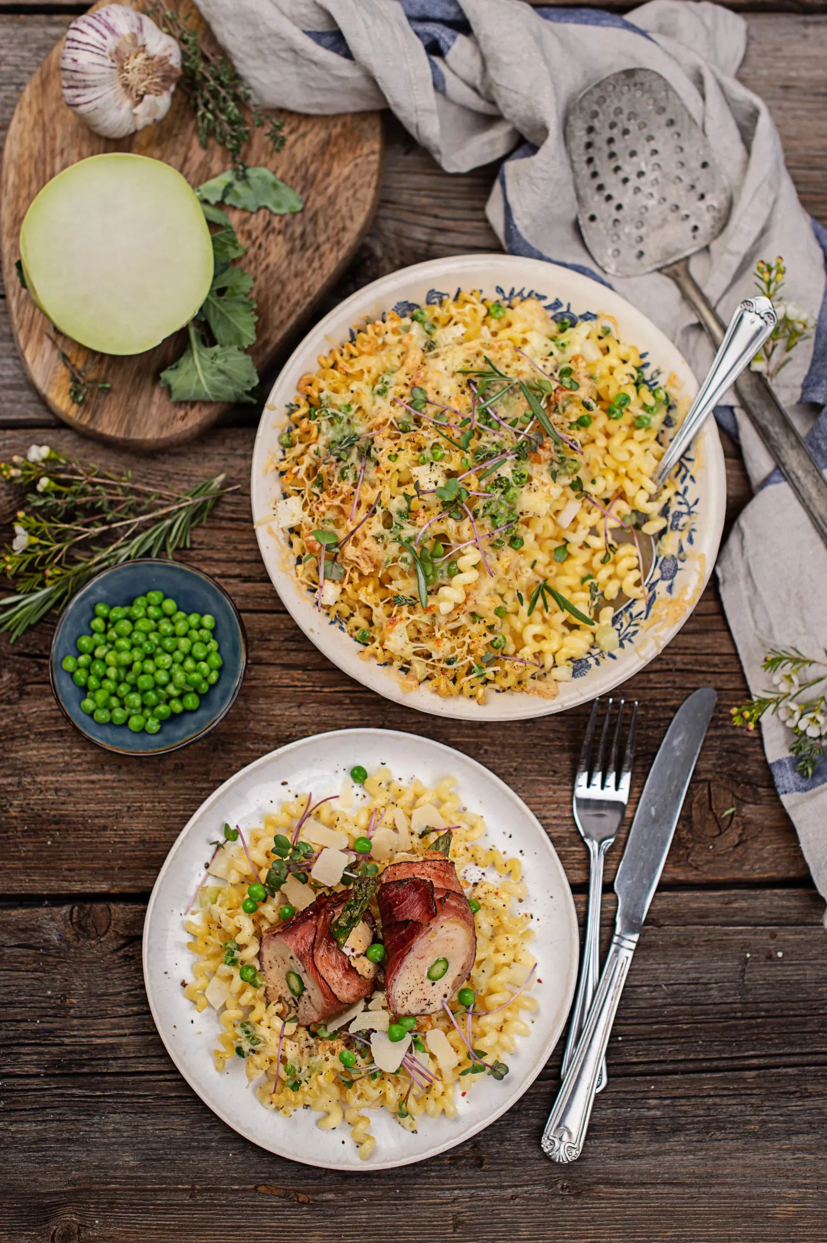 Kohlrabi-Nudel-Gratin mit Puten-Involtini, Nudeln und Erbsen, auf zwei Tellern auf rustikalem Holztisch