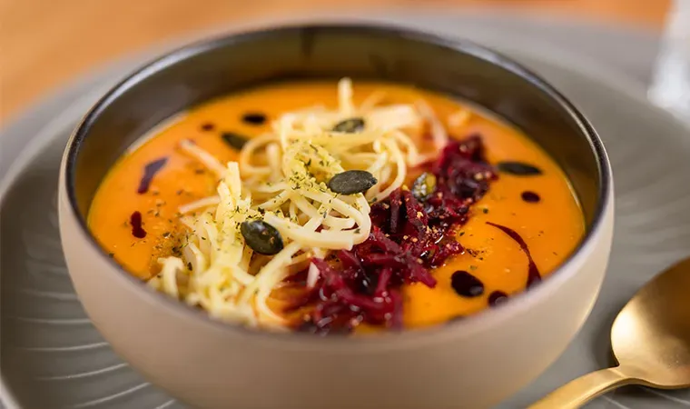Cremige Kürbissuppe mit Hausmacherschnitt in einer Schüssel, mit Käse und Streifen von Roter Bete garniert