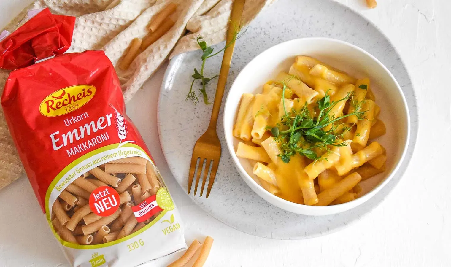Vegane Mac and Cheese mit Emmer-Makkaroni, Käsesauce und Kräutern in einer Schale neben einer Pastapackung
