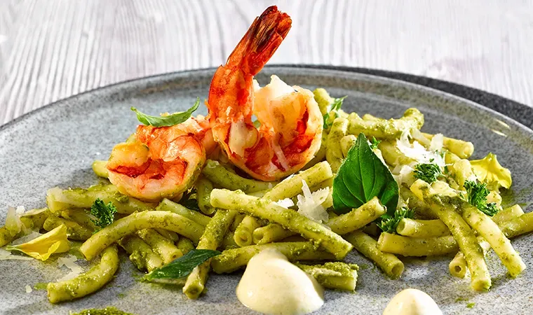 Maccaronelli mit Kräuterpesto, Pilzschaum und Alpengarnele, mit Basilikumblättern auf einem Teller