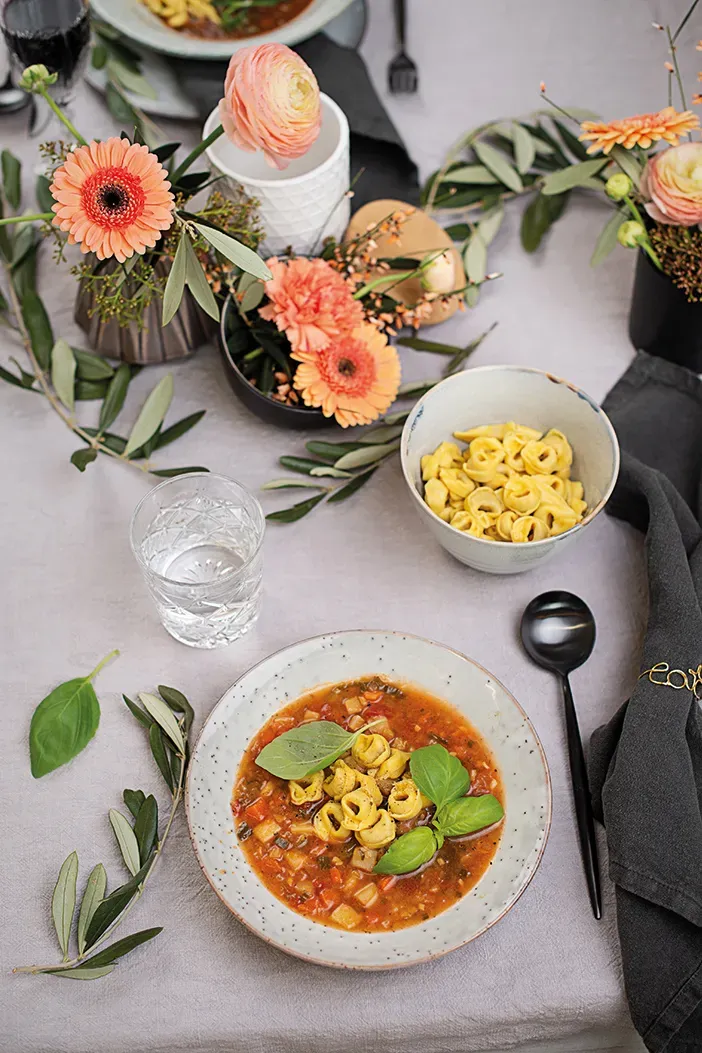 Minestrone mit Tortellini und Blumen auf Teller auf gedecktem Tisch
