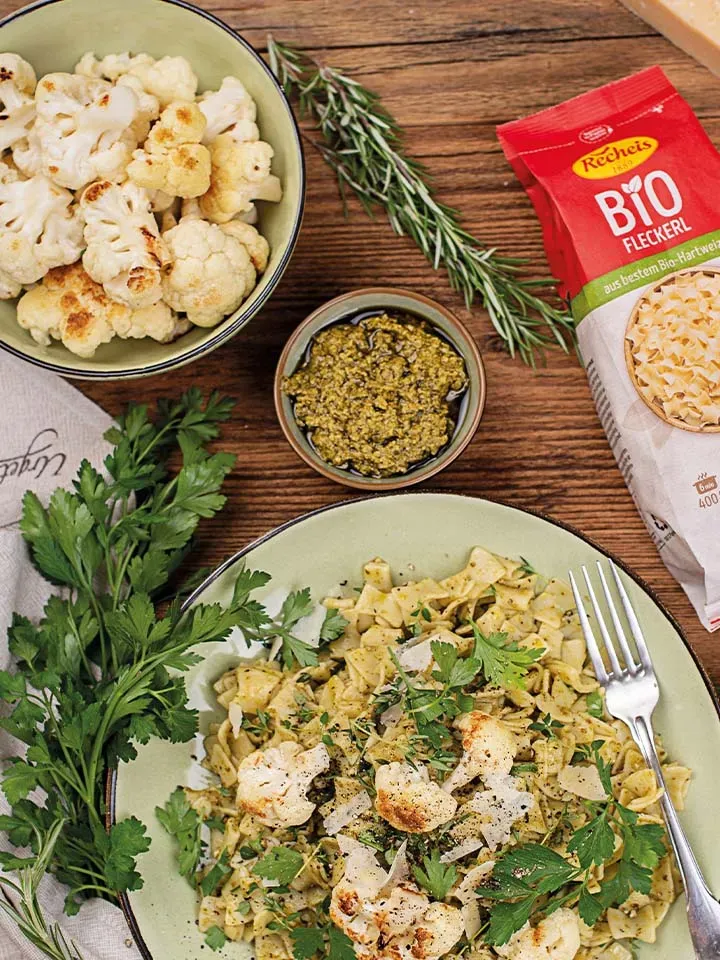 Fleckerl mit geröstetem Karfiol und Pesto auf einem Teller auf Holztisch neben der Pasta-Packung