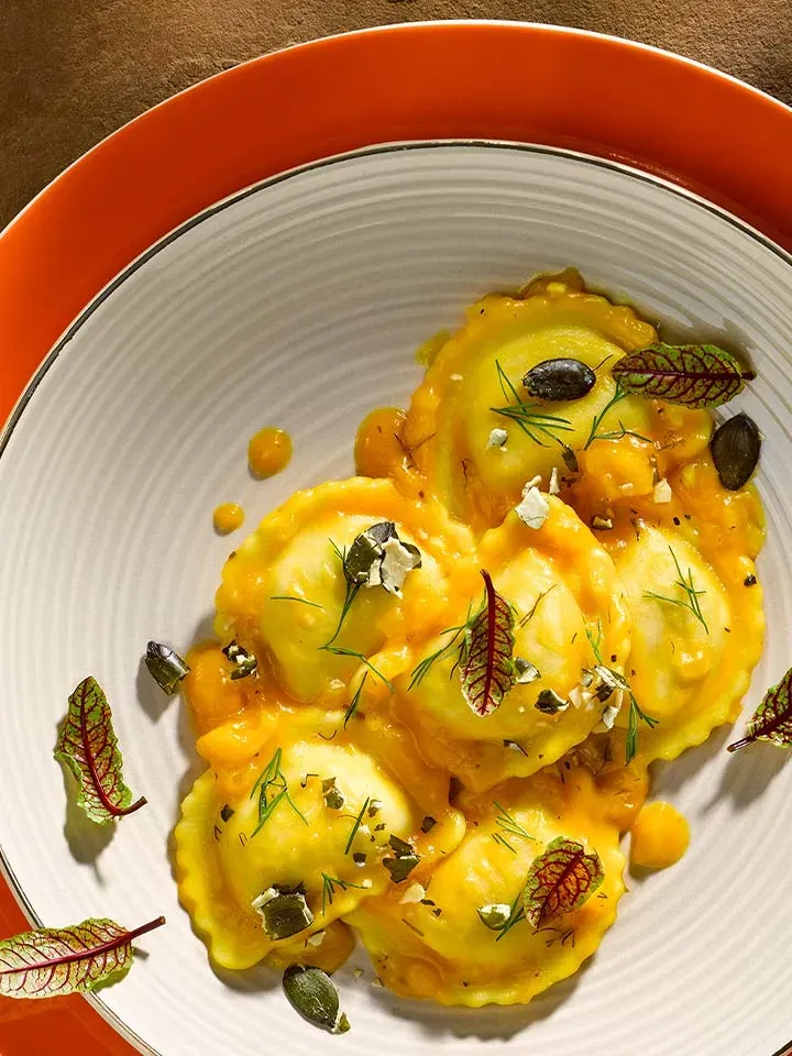 Fünf Mezzelune mit Kürbisconfit in orangener Sauce, garniert mit Kräutern und Samen