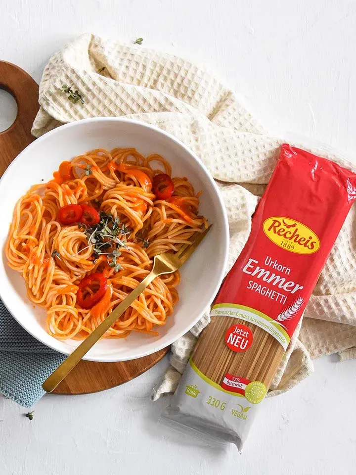 Spaghetti mit Paprika und Tomatensauce in einer Schale neben einer Packung Recheis Emmer Spaghetti