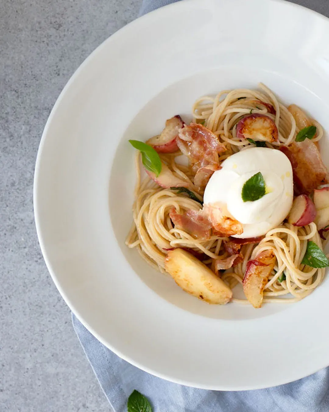 Pikante Spaghetti mit Pfirsich, Speck und Mozzarella, mit Basilikum garniert, auf einem Teller