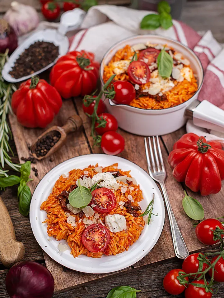 Nudel-Risotto mit frischen Tomaten, angerichtet auf einem Teller auf rustikalem Holztisch