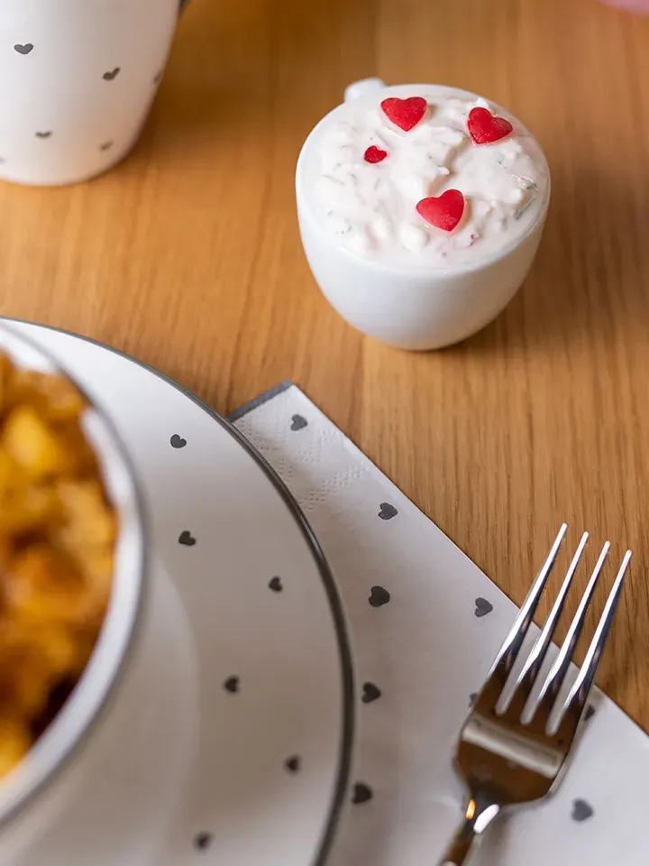 Nudelchips mit Radieschendip: kleine Schale mit weißer Creme und roten Herzdekorationen auf Holztisch