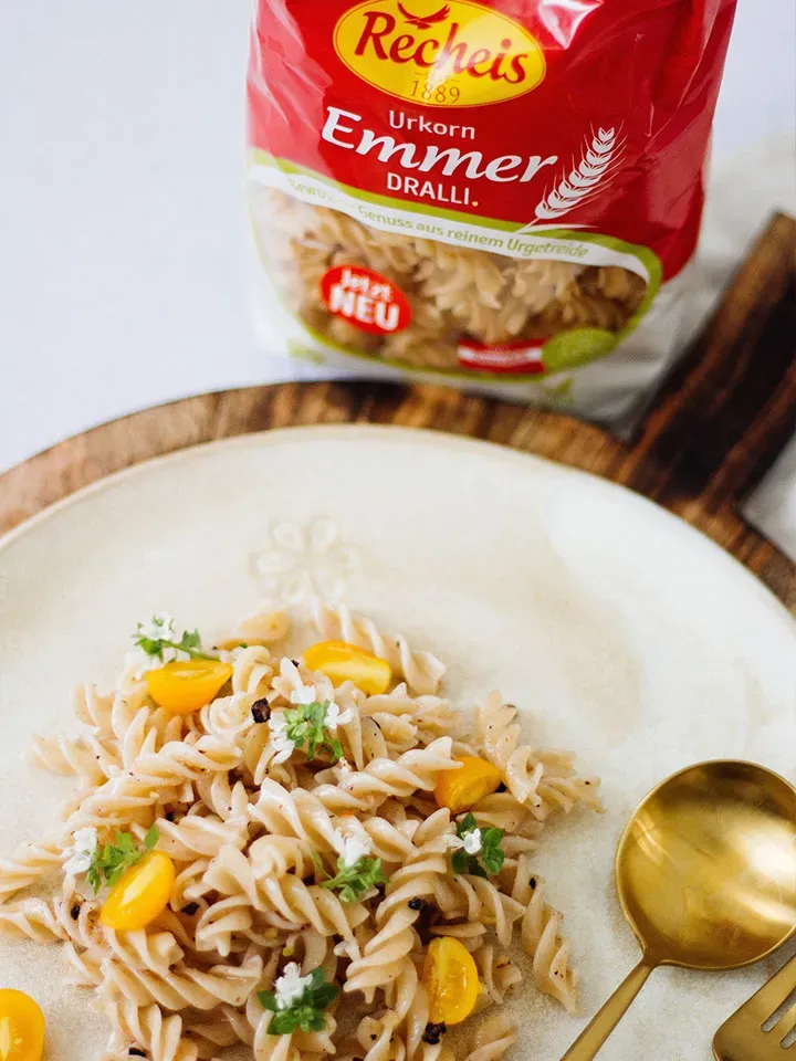 Emmer-Nudeln mit Aronia-Nuss-Pesto, gelben Tomaten und Kräutern auf Teller neben Emmer-Pastapaket