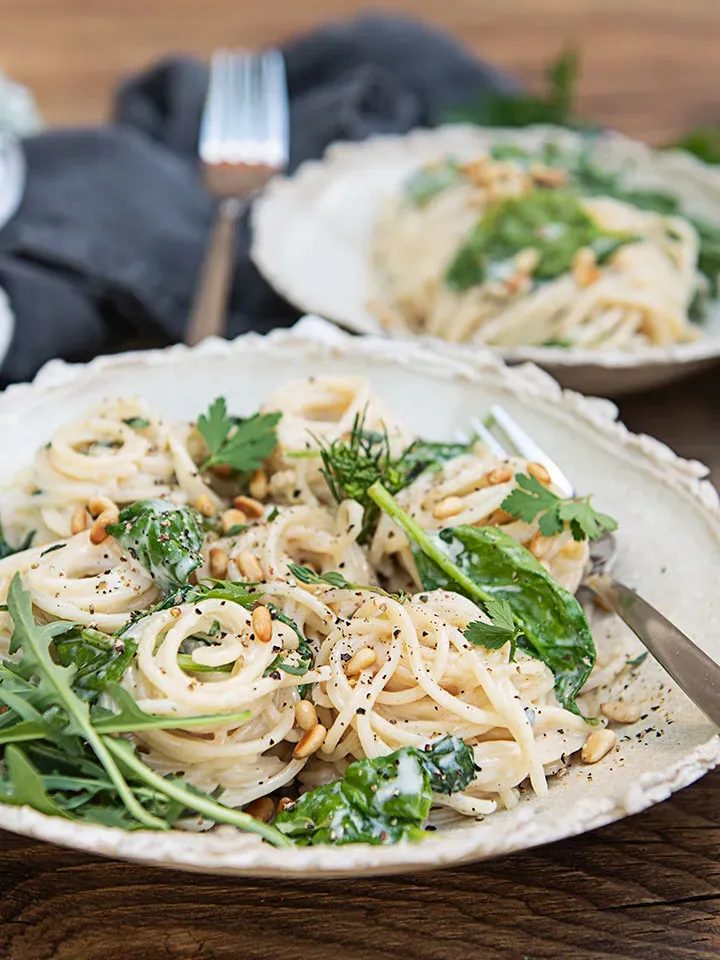 Spaghetti mit Gorgonzola, grünen Blättern und Pinienkernen auf einem Teller auf Holztisch