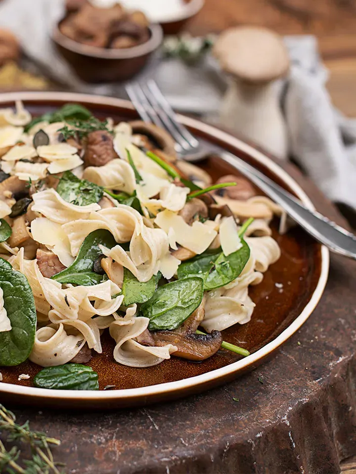 Nudelpfanne mit Pilzen und Kastanien, Spinat und Parmesan auf rustikalem Untergrund