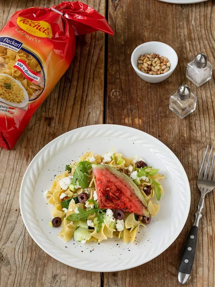 Nudelsalat mit gegrillter Wassermelone, Oliven und Feta auf Teller auf Holztisch mit Gewürzen