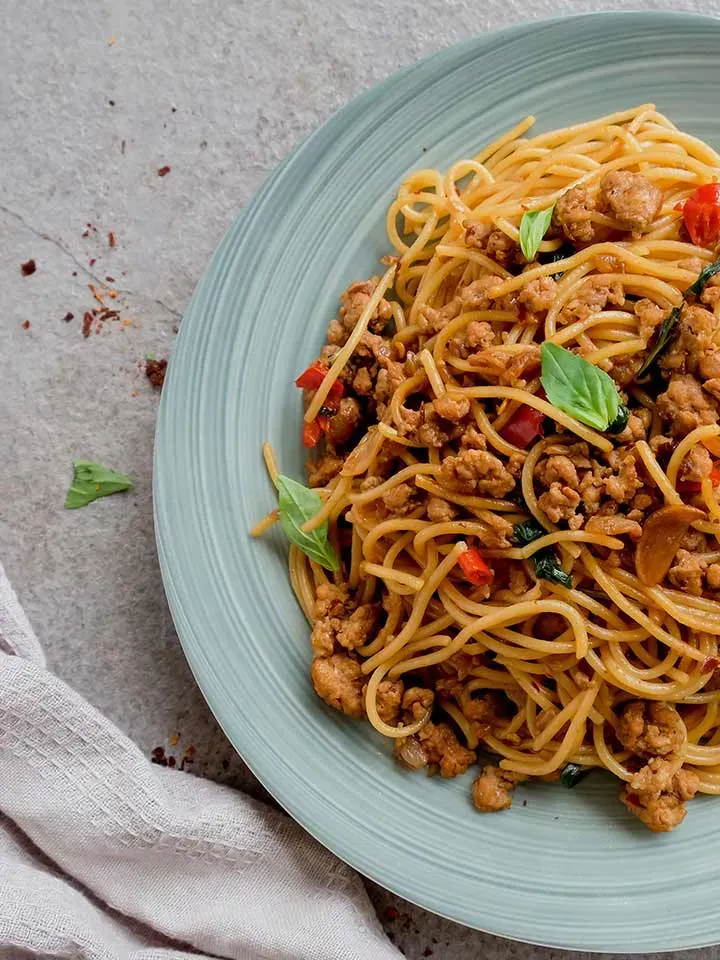 Pad Kra Pao mit Dinkelspaghetti und Hackfleisch, garniert mit Basilikumblättern, auf einem Teller