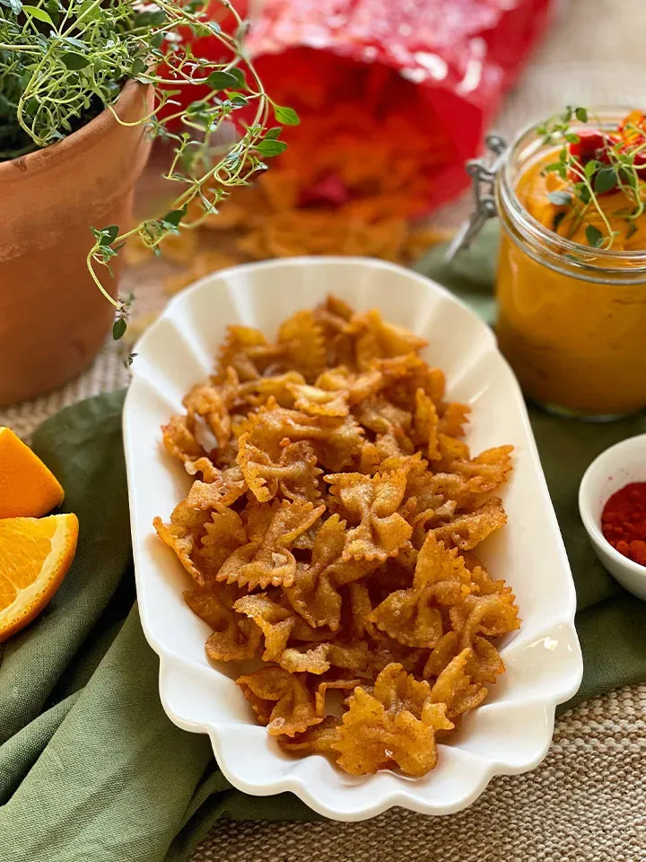 Frittierte Paprika-Nudelchips aus Farfalle mit selbstgemachtem Kürbisdip und Kräutern auf weißem Teller