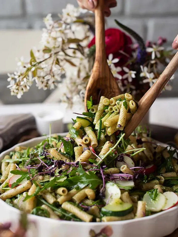Holzlöffel heben Nudelsalat mit Radieschen-Grünpesto, Gemüse und Kräutern aus einer Schüssel